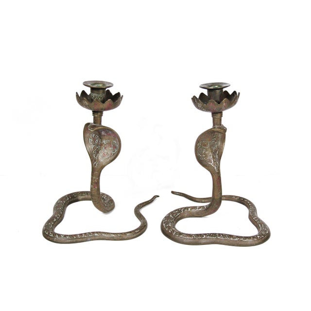 A dramatic pair of vintage brass cobra snake candleholders with hand-engraved decorative patterns and lotus-style candle...