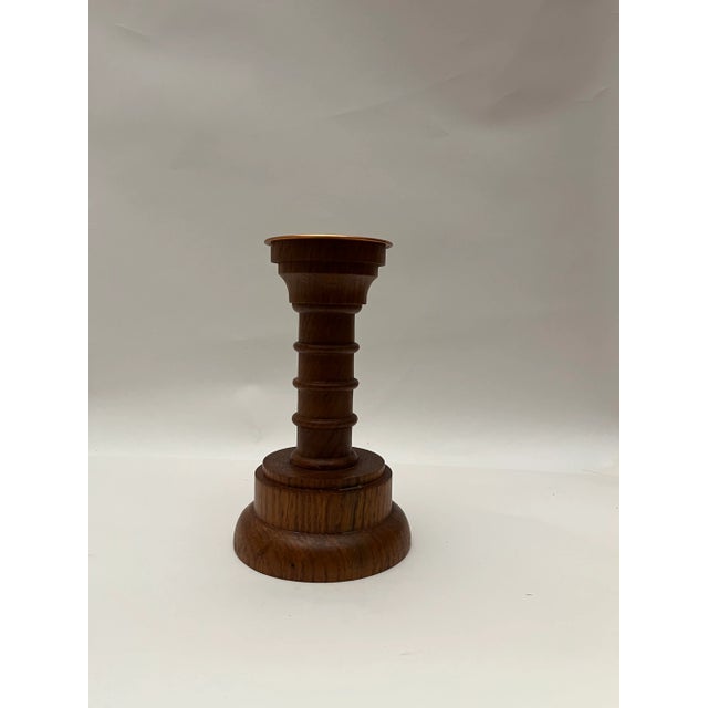 This is a Danish wooden candlestick holder with a copper-colored metal cup at the top. The candlestick has a turned design.