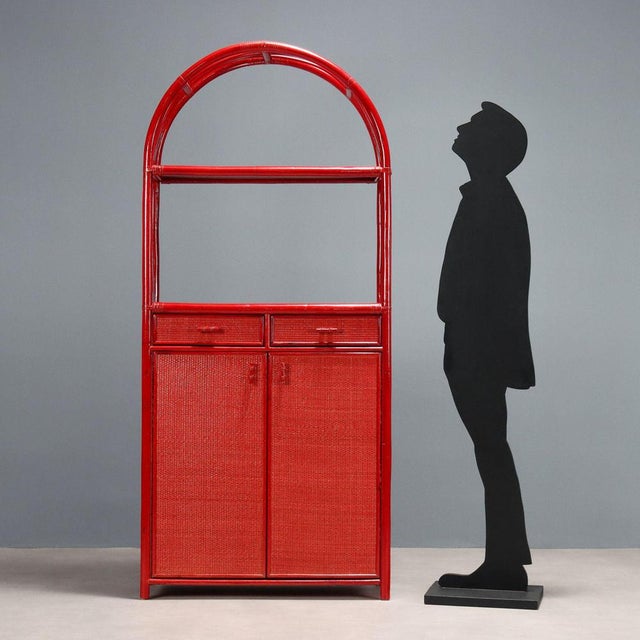 Vintage bookcase made of red enamelled bamboo with hinged doors, drawers and wicker shelf with glass top. This piece is...