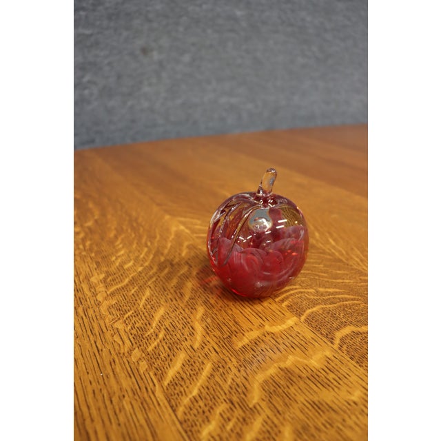 Hand-blown art glass paperweight in the form of an apple with a rich cranberry red body, clear overlay, and applied clear...