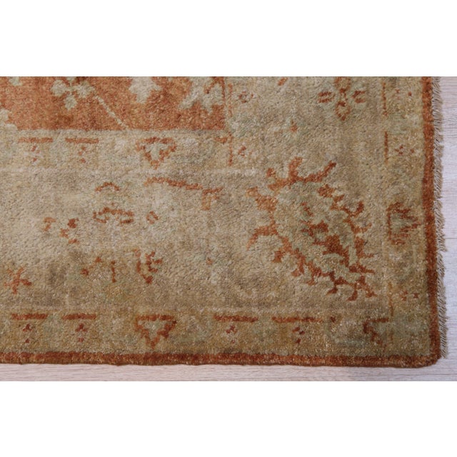 A 10' x 14' hand-knotted wool rug with a rust and terracotta allover floral design on a gold ground, with natural color...