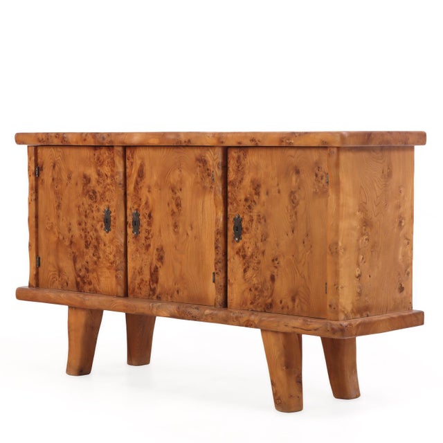 A striking French Brutalist style burl elm buffet, dating to circa 1960, showcasing the dramatic natural beauty of richly...