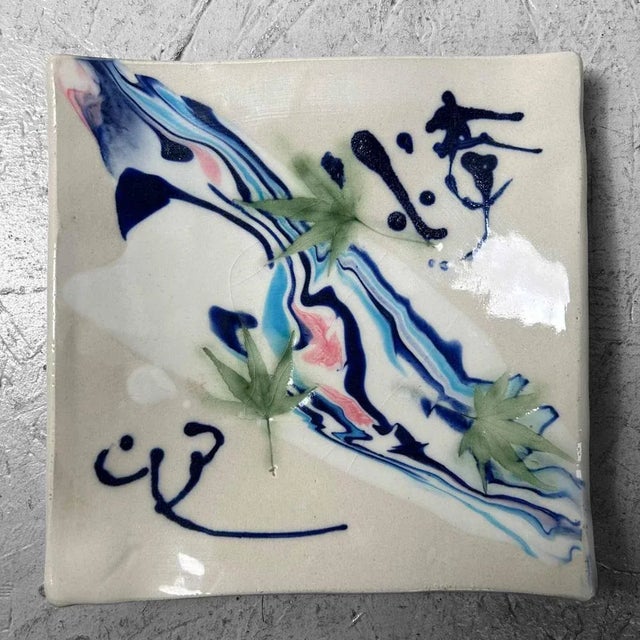 Striking small dish/vide-poche on four legs. Decorated with a calligraphy-like script, a Japanese maple leaf motif, and...