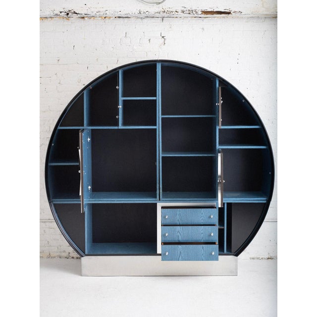 An Italian Space Age wall unit. Laminate blue faux bois with black lacquer, glass and aluminum details. A diverse storage...