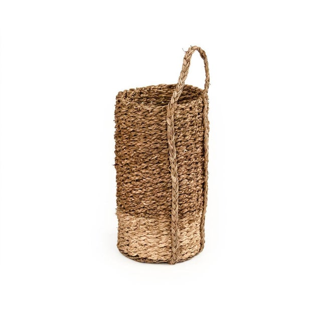 Cylindrical woven handmade seagrass basket with a woven handle and beige bottom.