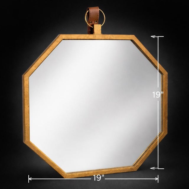 A refined octagonal brass-framed wall mirror featuring a leather strap and ring detail. Warm metal tones and clean...