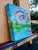 This artwork presents a close-up of an eye reflecting a serene landscape, where vibrant greens and blues meld seamlessly....