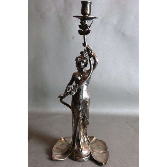 Pair of Art Nouveau silver-plated bronze candlesticks depicting women holding vines (one leaf missing). Monogram on the...