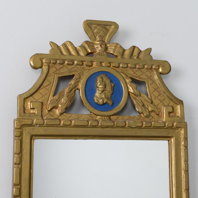 A Gustavian mirror measuring 75 cm x 35 cm. The piece is bronzed and features a blue-ground cameo. Arches and patterns are...