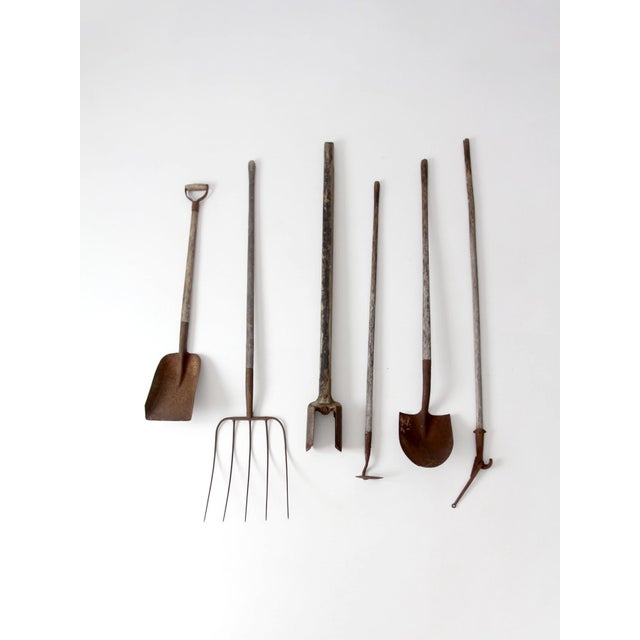 A collected set of early 20th century farm and garden tools featuring worn wood handles and aged metal heads, including a...