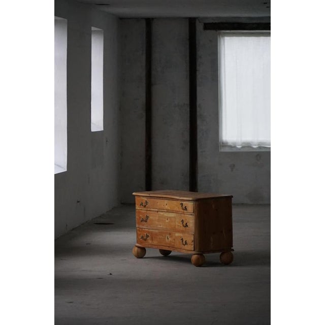 A charming antique chest of drawers crafted in solid pine, featuring a gently curved front and beautifully aged surface...