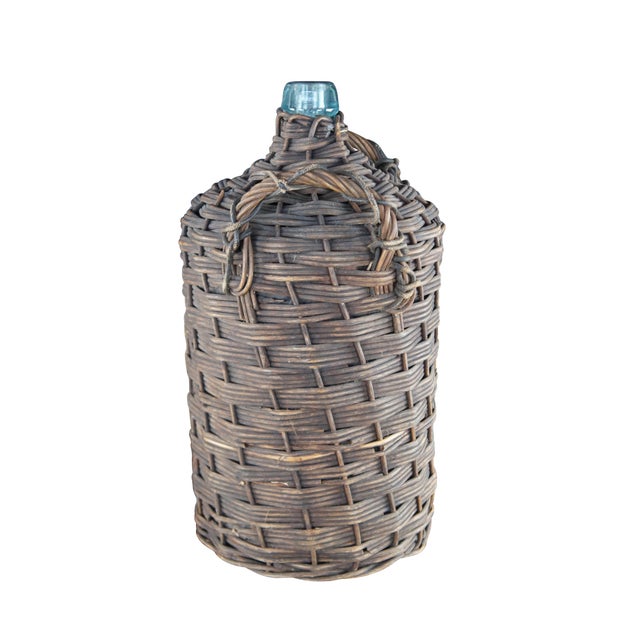 An early 20th-century green glass wine bottle/ demijohn or carboy, fully wrapped in woven wicker with handles. No cork....