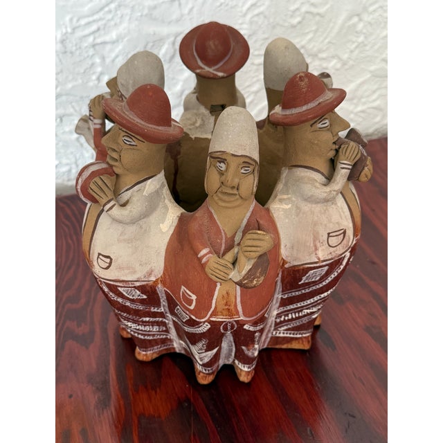 This handmade terracotta whistle sculpture shows a ring of Andean musicians in brimmed hats, each playing a traditional...