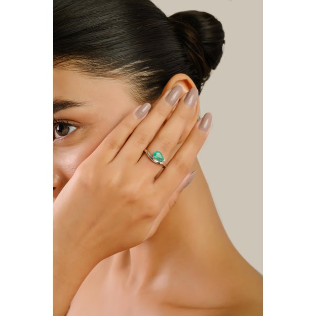 This elegant wave ring features a pear-cut Zambian emerald weighing 1.31 carats, set in 14K solid white gold. The vibrant...