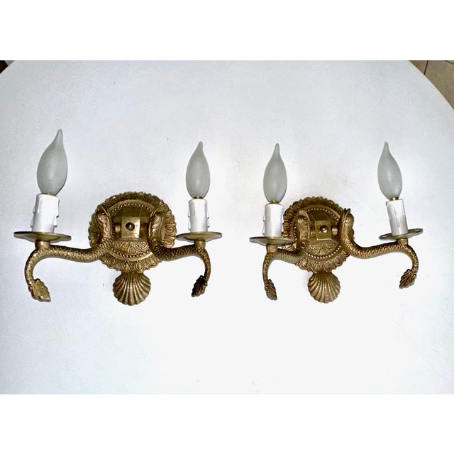 Pair of European two-light neoclassic style brass wall sconces with dolphin and claim shell motif. Expertly crafted with...