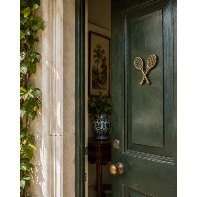 A charming 1970s cast brass door knocker modeled as a pair of crossed tennis rackets, complete with textured stringing and...