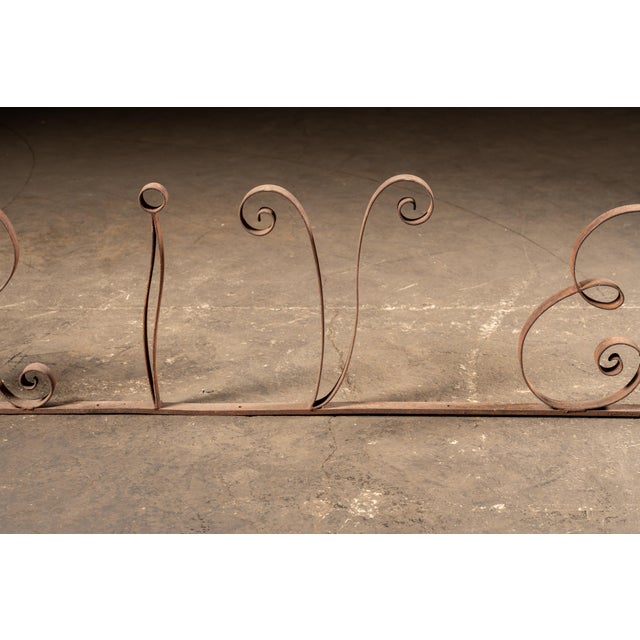 A full-length, hand-forged iron "DRIVE-IN" sign rendered in scrolling bar stock with generous loops, tight curl...