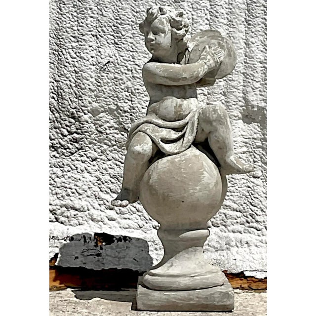 This charming vintage Regency cast concrete figural sculpture features a whimsical depiction of a cherub seated atop a...