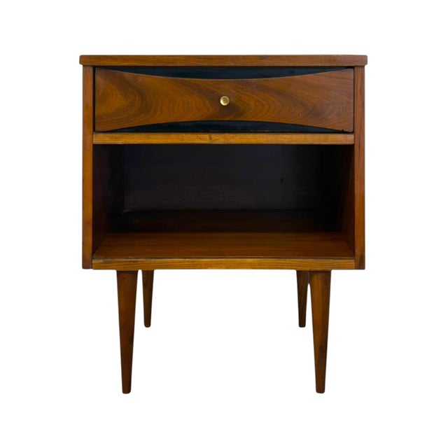 This mid-century modern nightstand features rich walnut wood tones, smooth grain patterns, and iconic tapered peg legs....