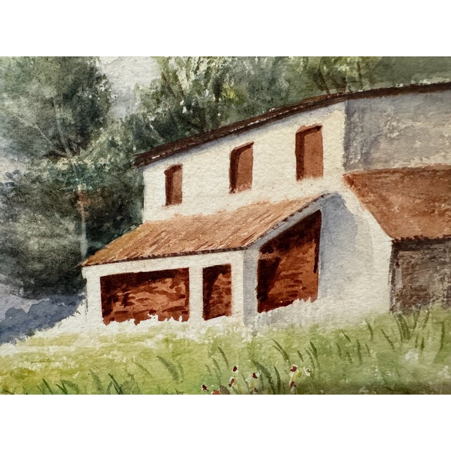 Original watercolor on textured paper depicting a white country house with warm red-brown roofs set beside a lush green...