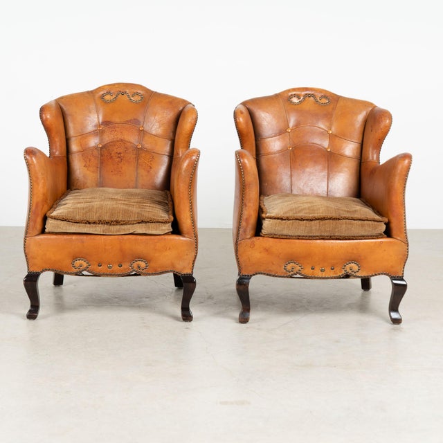 Pair of early 20th-century vintage leather club chairs with decorative nail head trim, self-piping and hardwood cabriole...