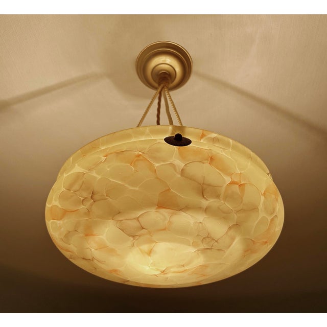 Art Deco pendant light with a light amber mottled glass shade with orange grey streaks, mounted on a braided multicolor...