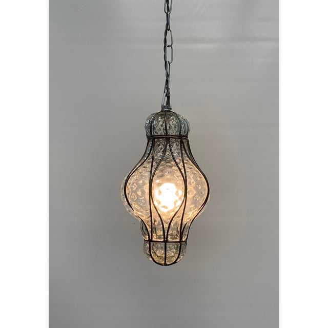 Medium-sized Murano glass hanging lantern, elegantly decorated with a gray, curly brass frame surrounding a finely...
