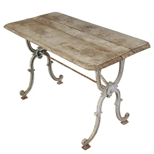 A charming French bistro or garden table featuring an ornate cast iron base with scrolling legs and a naturally weathered...