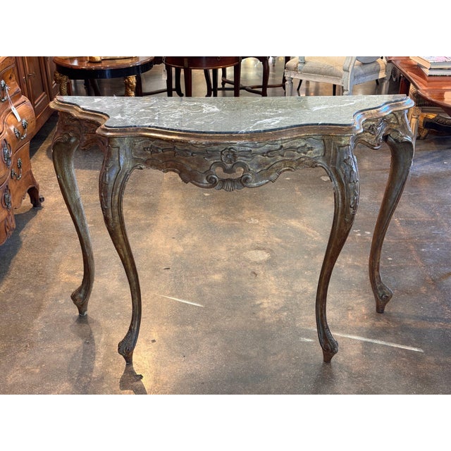 Serpentine grey veined marble top sits on a carved 19th century French giltwood frame, the shaped apron centered by a...
