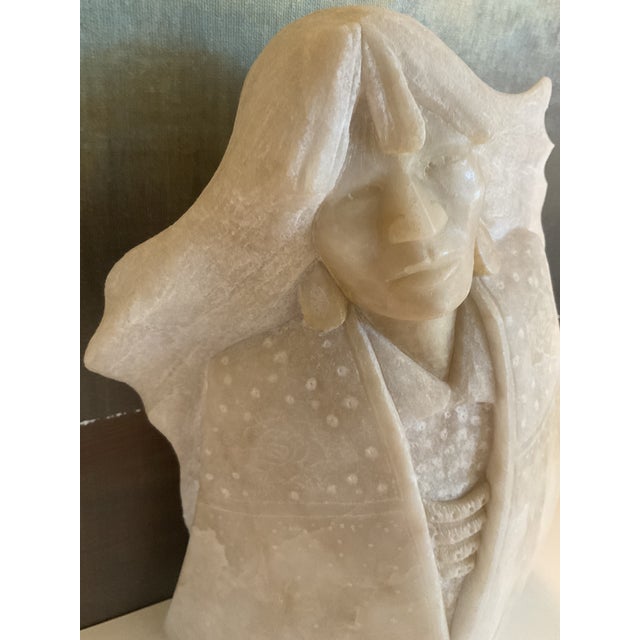 Hand-carved alabaster sculpture depicting a stylized figure in a flowing garment. Material: Alabaster (light cream to...