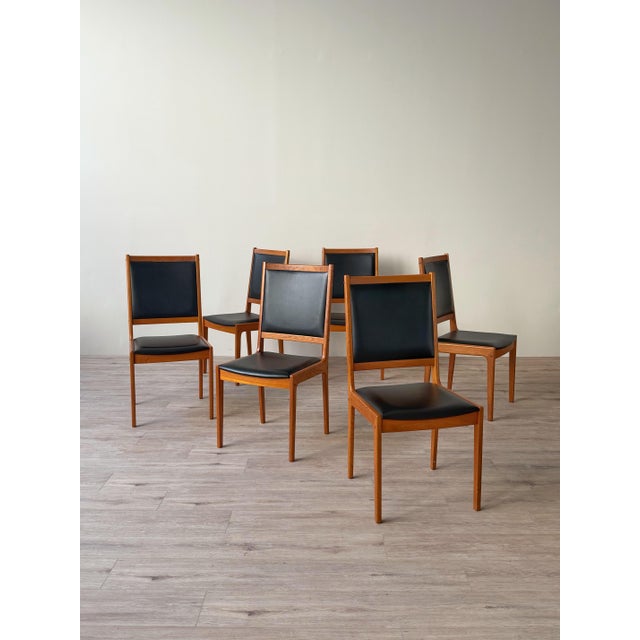 Set of six vintage Danish dining chairs featuring teak frames with tall upholstered backs and padded seats in black vinyl...