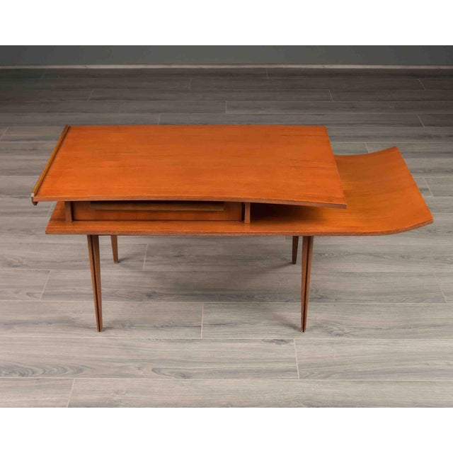 A sculptural mid-century occasional table in walnut veneer, its top tier finished with a raised back edge and a sweeping...