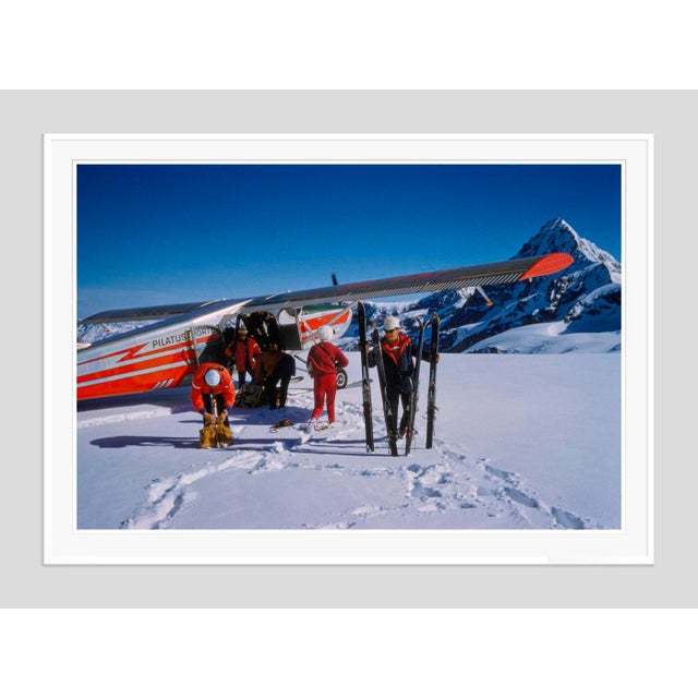 Landing At The Haute Route by Toni Frissell A group of skiers wait by the side of a ski plane at the top of a piste in...