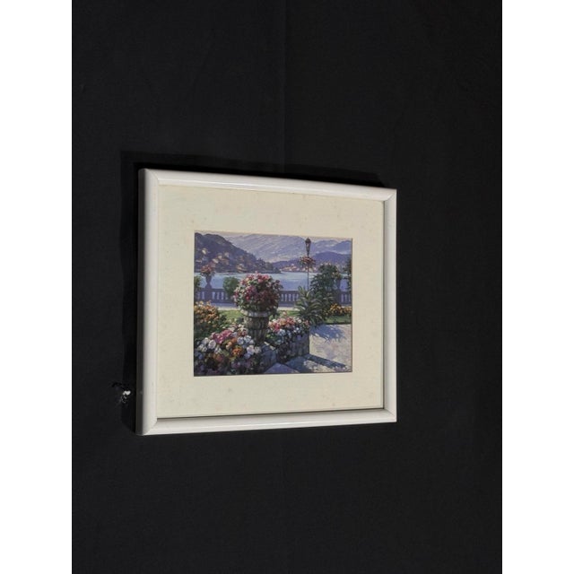 Framed landscape print of a colorful flower garden above a quiet lake with distant mountains. The soft palette gives it a...