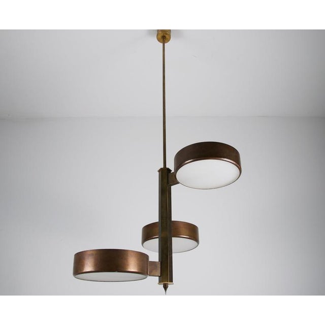 This refined three-light pendant features a vertical brass structure with staggered circular shades arranged at different...