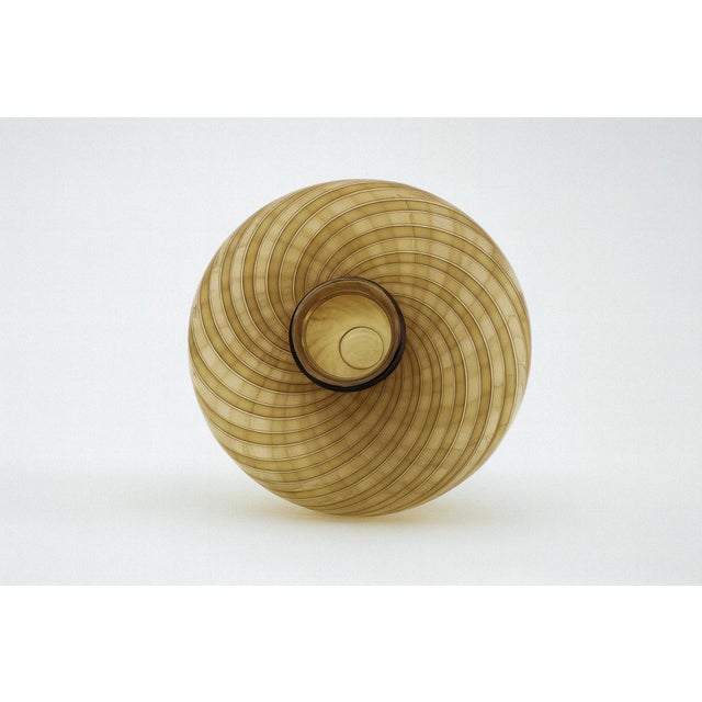 A glass vase defined by a fluid spiral pattern in gold and brown. Its transparent body enhances the sense of movement,...