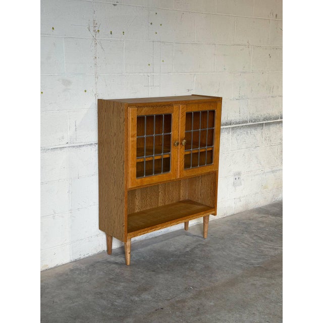 This charming storage piece features glass-paned upper doors with detailed leading and an open lower shelf. Supported by...