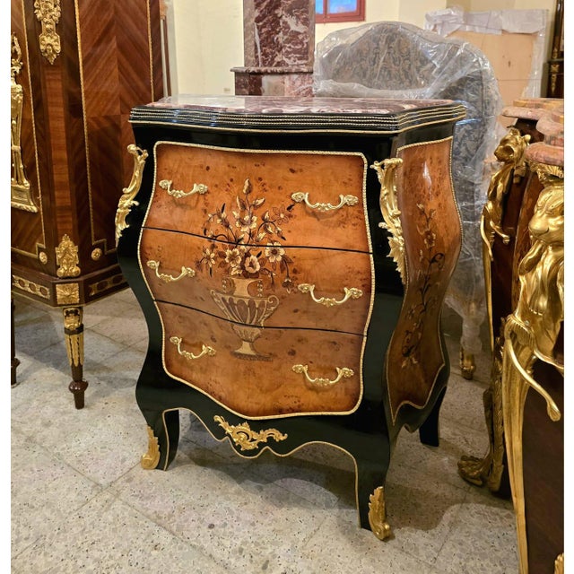 Magnificent French Rococo-style commode chest featuring an elegant curved silhouette, luxurious marble top, and richly...