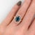 A blue zircon glows in a brilliant electric blue at the heart of this solid 14K rose gold ring, flanked by thirty-two...