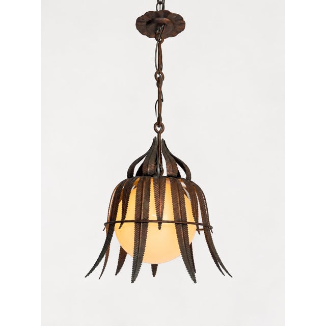An unusual Spanish pendant light from the 1950s, featuring hand-worked, copper-plated iron leaves arranged around a white...