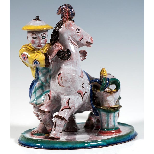 An exotic decorated, restlessly looking horse stands on an oval base plate; a chinese man with typical headgear looks out...