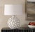 The Hartley Table Lamp features a ceramic base adorned with layered petals in a warm white glaze, accented with antique...