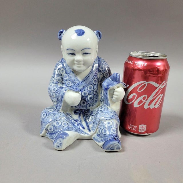 Very nicely hand painted porcelain seated Chinese boy holding a lingzhi fugus, traditional symbol of longevity, in his...