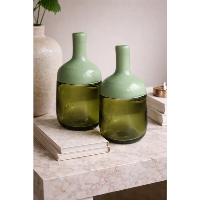 A beautifully crafted pair of handmade art glass bottles featuring a sophisticated two-tone green palette. Each piece...
