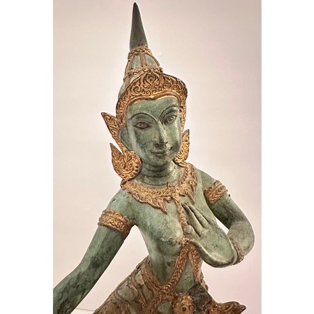 A large bronze sculpture of a seated figure rendered in a classic Thai or Southeast Asian style, with a tall, pointed...