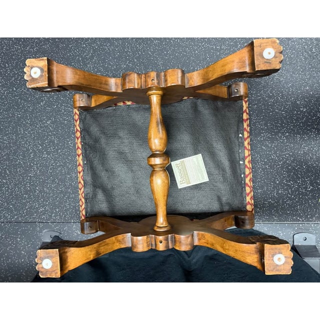 Ornate ottoman has a dark-stained wood base with intricate carvings. The base features an X-frame design with a central...