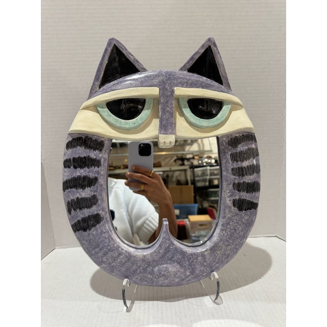 Whimsical sculptural cat-form wall mirror dated 1981, with lavender-gray body, black striped detailing, cream face, pale...