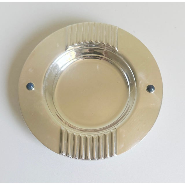 A sophisticated silver-plated catchall or ashtray by Cartier. The rim features fluted rests and two vivid blue lapis...