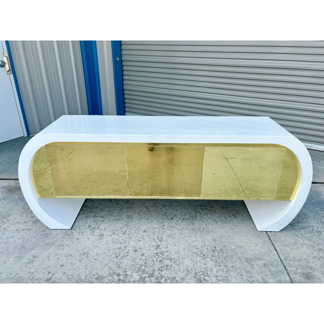 Mid-century curved lacquer and brass credenza designed and manufactured in the United States circa 1970s. This exquisite...