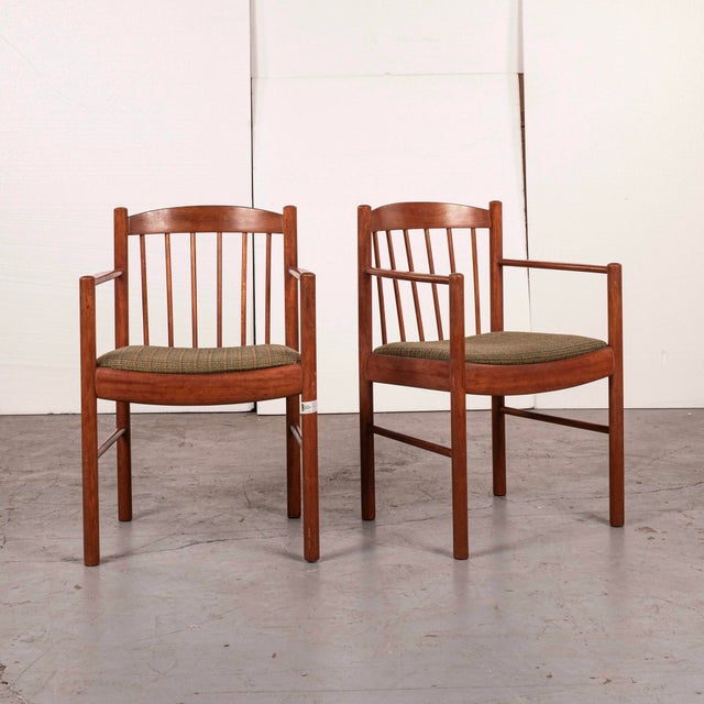 Danish modern teak dining chairs with curved crest rails, vertical spindle backs, and upholstered floating seats. The...